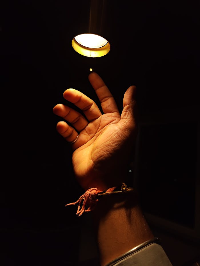 A hand reaching toward a warm circular light source in a dark room, invoking hope.